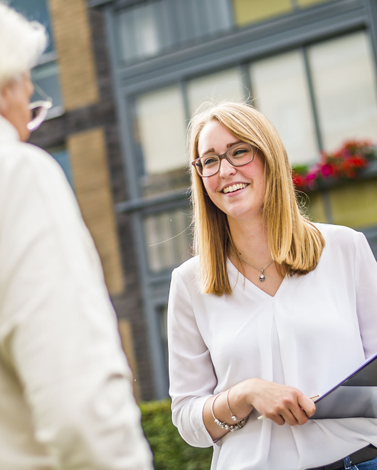 Freundlich lächelnde Mitarbeiterin im Gespräch mit einer Mieterin.