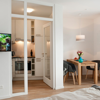 Blick in den hellen Raum: Flachbildfernseher an der Wand, rechts Esstisch mit zwei Stühlen, dazwischen der Blick in die Küche. Blick in den Raum: Flachbildfernseher an der Wand, rechts Esstisch mit zwei Stühlen, dazischen der Blick in die Küche.