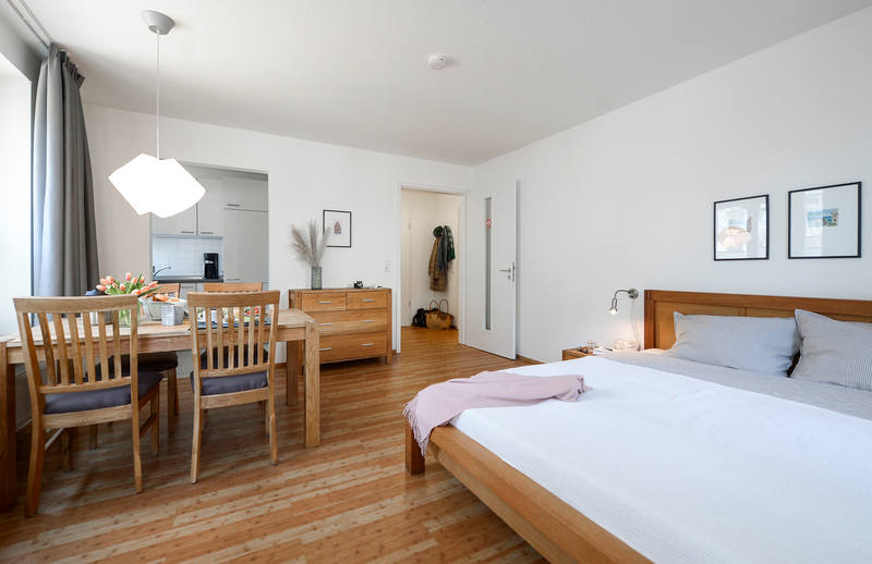 Wohnraum einer Gästewohnung mit Doppelbett, Esstisch und offener Küchenzeile